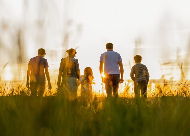 Rear view of family with three children walking on grass field during sunset
